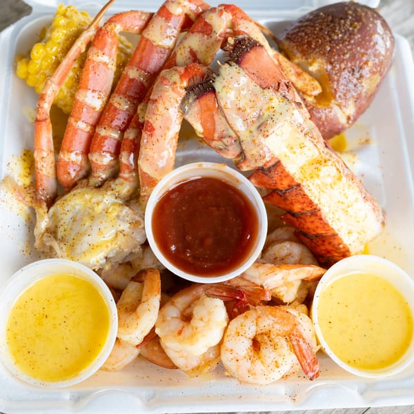 A seafood boil with crab legs, shrimp, corn on the cob, and potatoes, served with dipping sauces.