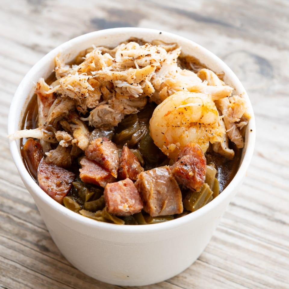 Close-up of a white bowl filled with gumbo, topped with shrimp, sausage, and crab meat.