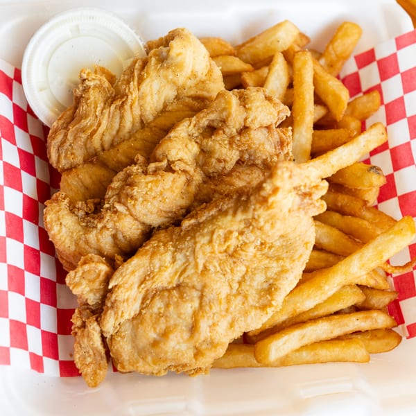 Crispy fried chicken tenders and golden french fries in a red and white checkered paper-lined container.