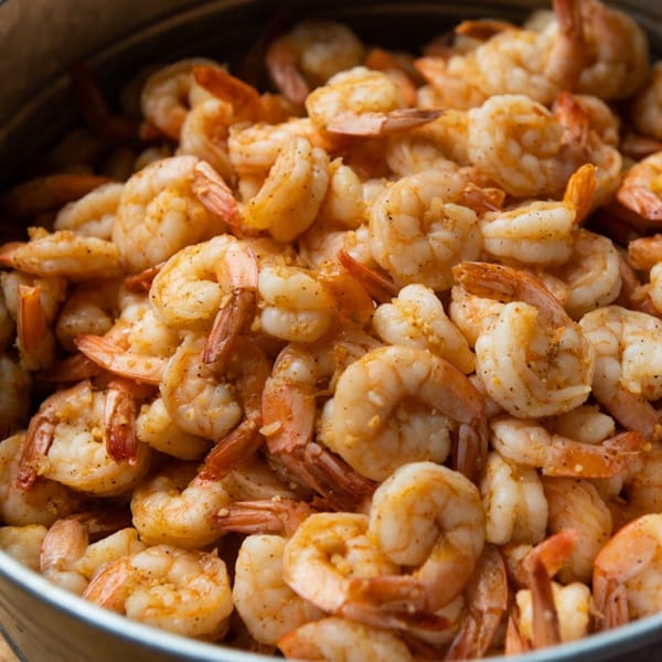 Close-up of a large serving of seasoned, cooked shrimp in a metal bowl.