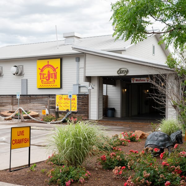 Exterior of Te'Jun Texas Cajun restaurant with a "Live Crawfish" sign and decorative landscaping.