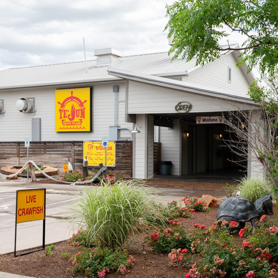 Exterior of Te'Jun Texas Cajun restaurant with a "Live Crawfish" sign and decorative landscaping.