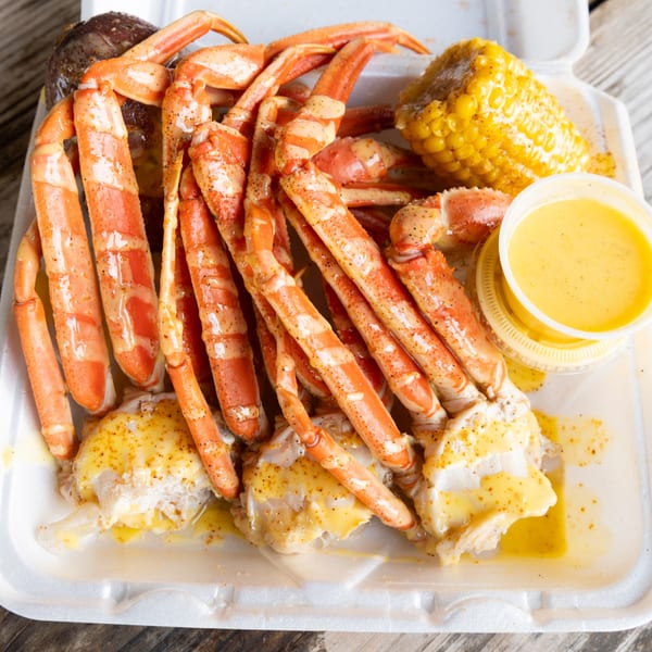 Snow crab legs, corn on the cob, and butter sauce in a white takeout container.