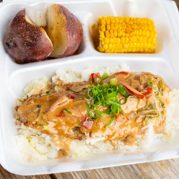 A takeout container with fish and rice, corn on the cob, and a baked potato.