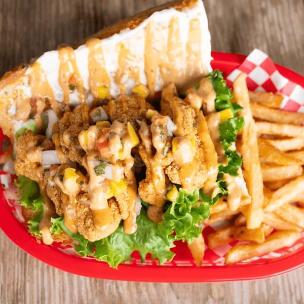 Crispy fried shrimp po'boy with lettuce, sauce, and fries in a red basket on a wooden table.