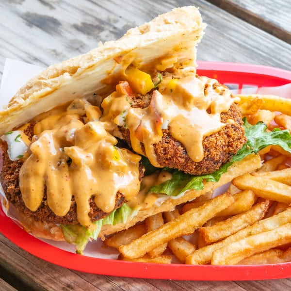 Crispy fried chicken sandwich with lettuce, sauce, and fries in a red basket on a wooden table.