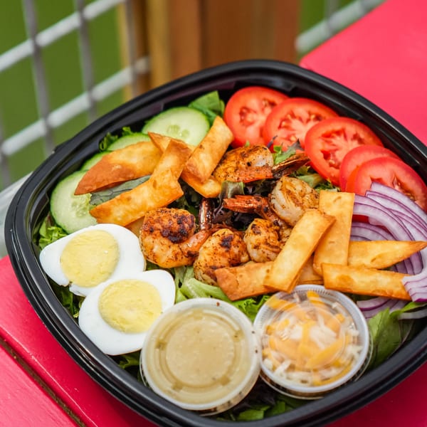 A vibrant salad with grilled shrimp, sliced tomatoes, cucumbers, hard-boiled eggs, and crispy wontons.