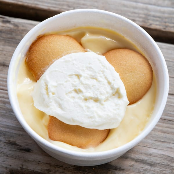 Banana pudding with vanilla wafers and whipped cream in a white bowl on a wooden surface.