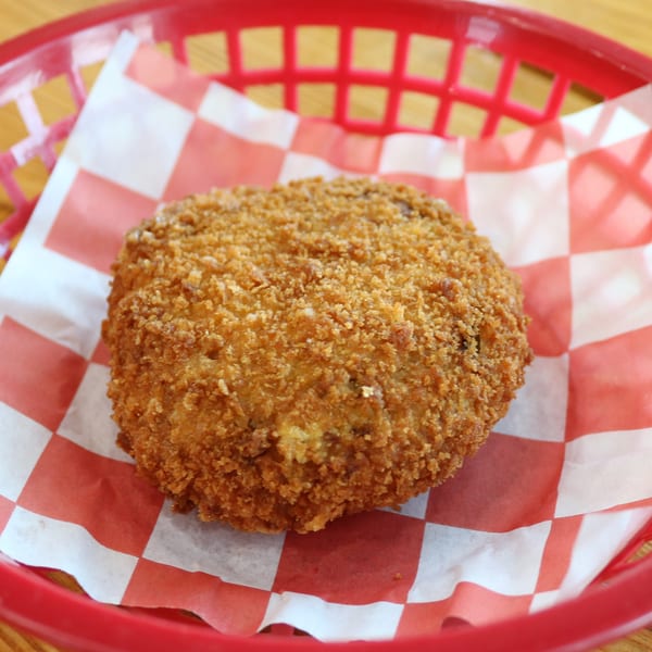 A golden-brown fried croquette in a red plastic basket lined with red and white checkered paper.
