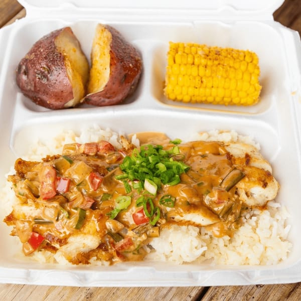 Fried fish with creamy sauce, rice, red potatoes, and corn on the cob in a takeout container.