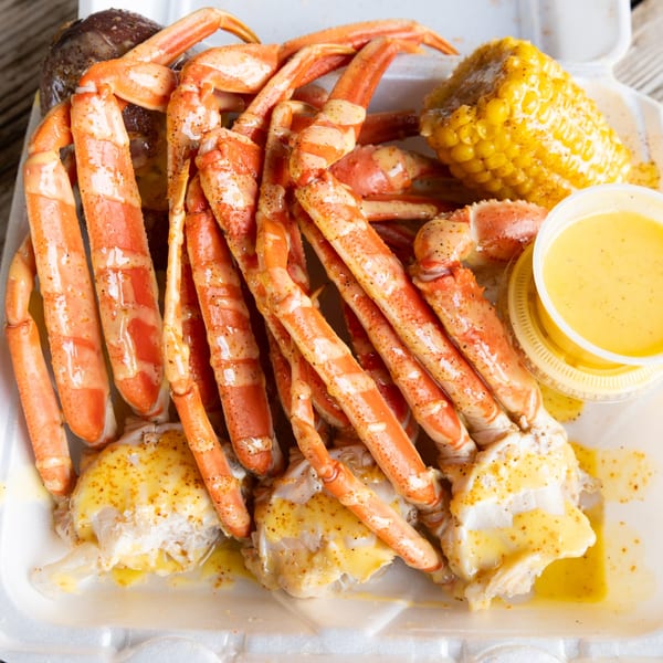Snow crab legs, corn on the cob, and melted butter in a white takeout container.