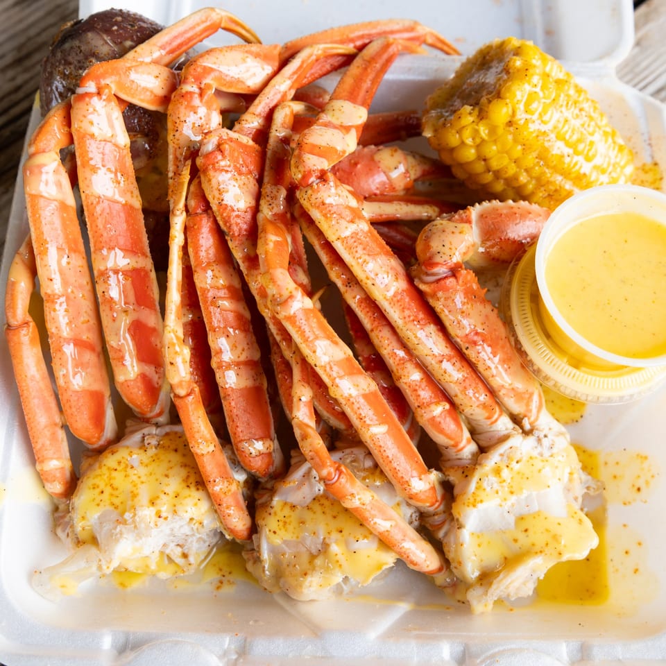 Snow crab legs, corn on the cob, and melted butter in a white takeout container.