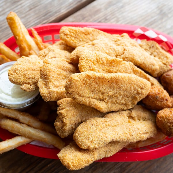 Fried fish fillets, french fries, and hush puppies in a red basket with tartar sauce.